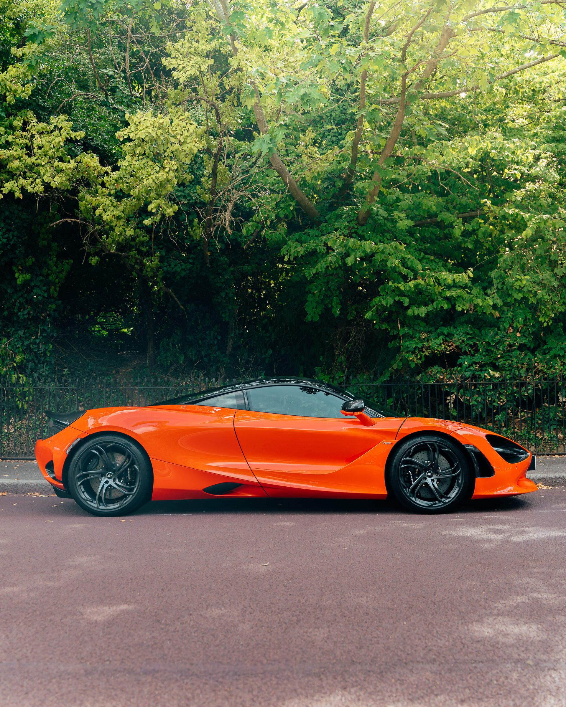 Orange McLaren 720S side profile beside trees