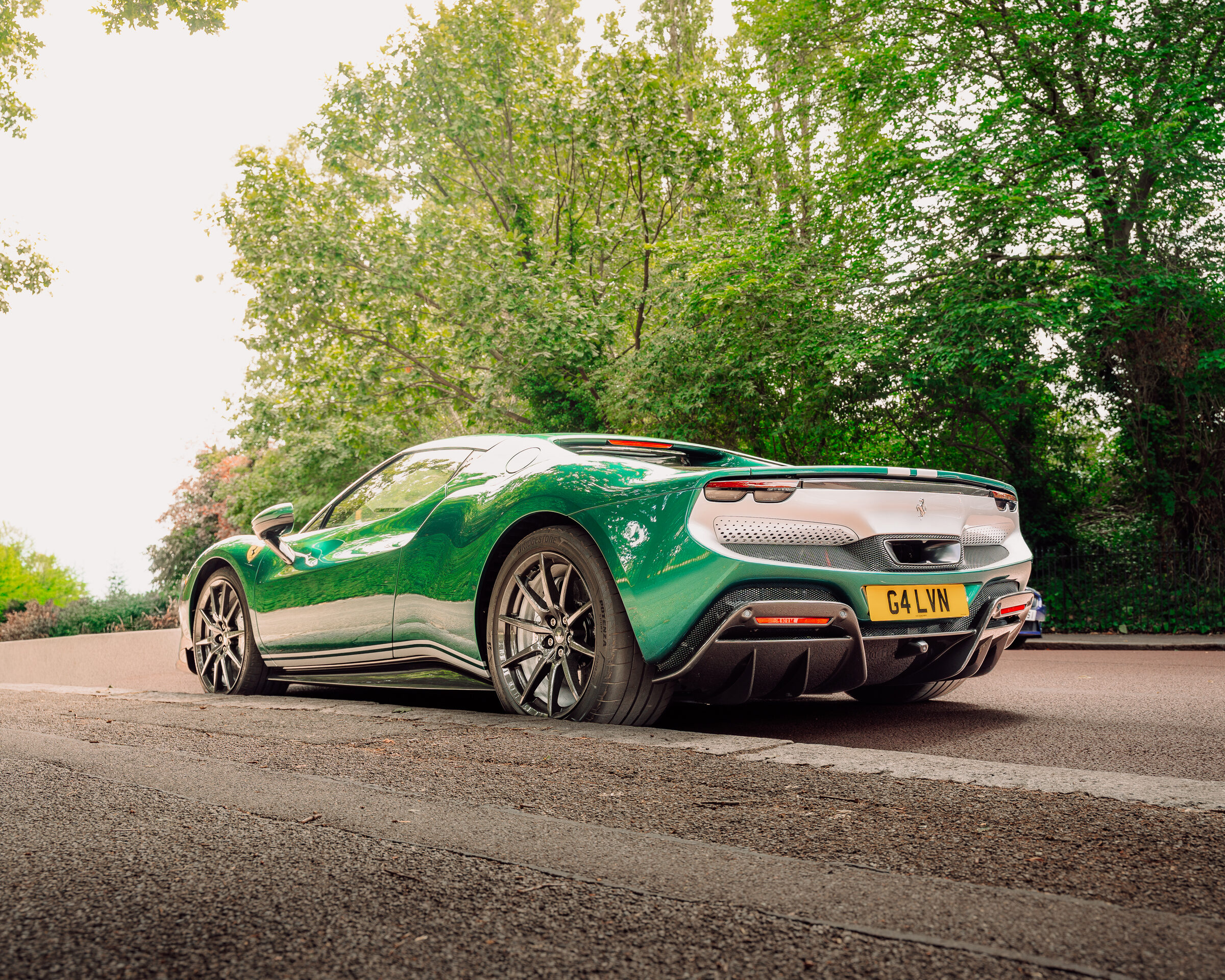 Green Ferrari 296 GTB rear three-quarter shot on a tree-lined road